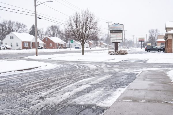 A cleared commercial concrete sidewalk and asphalt parking lot showing winter ice mitigation and slush control after a lake-effect snowstorm in Buffalo, New York.